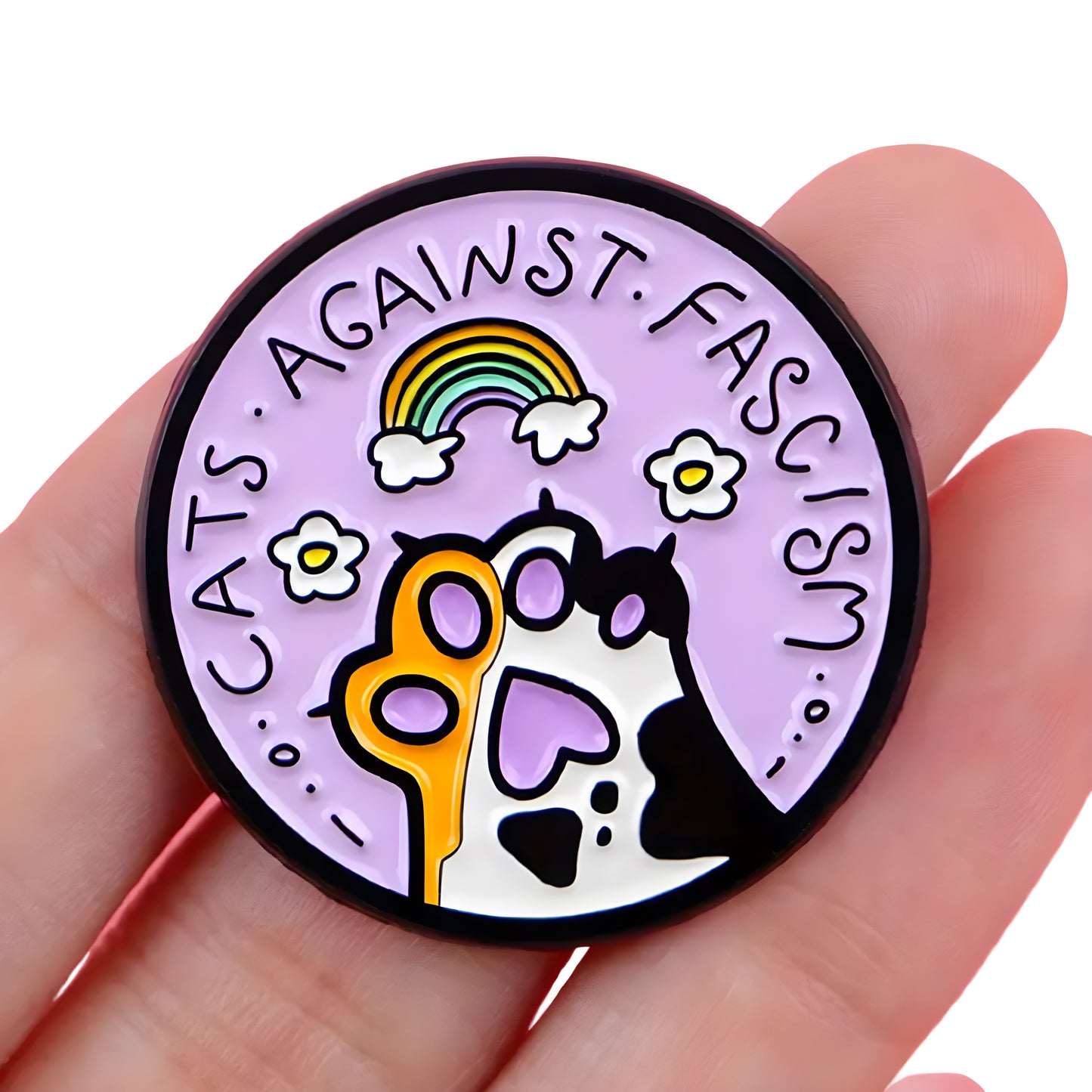 Pastel enamel pin reading “Cats Against Fascism” with rainbow and cat paw artwork held in a hand