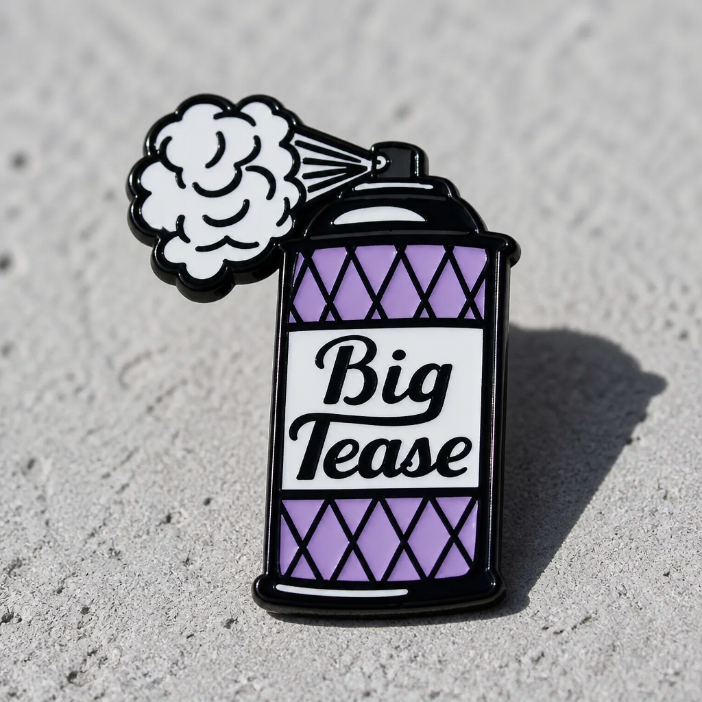 Enamel pin shaped like a retro spray can labeled Big Tease with a puff of spray coming from the nozzle on a concrete surface