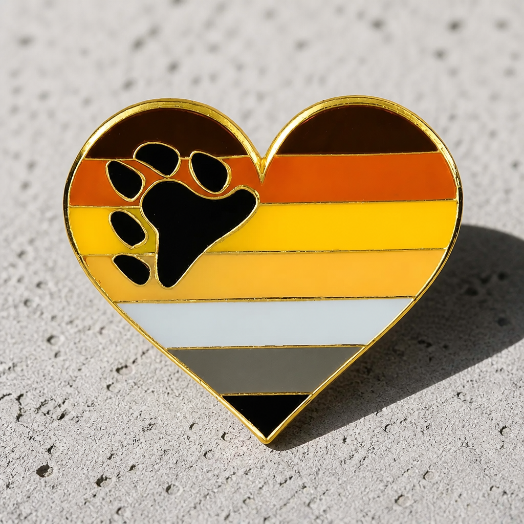 Heart-shaped Bear Brotherhood enamel pin with paw print and bear Pride flag colors on a concrete background