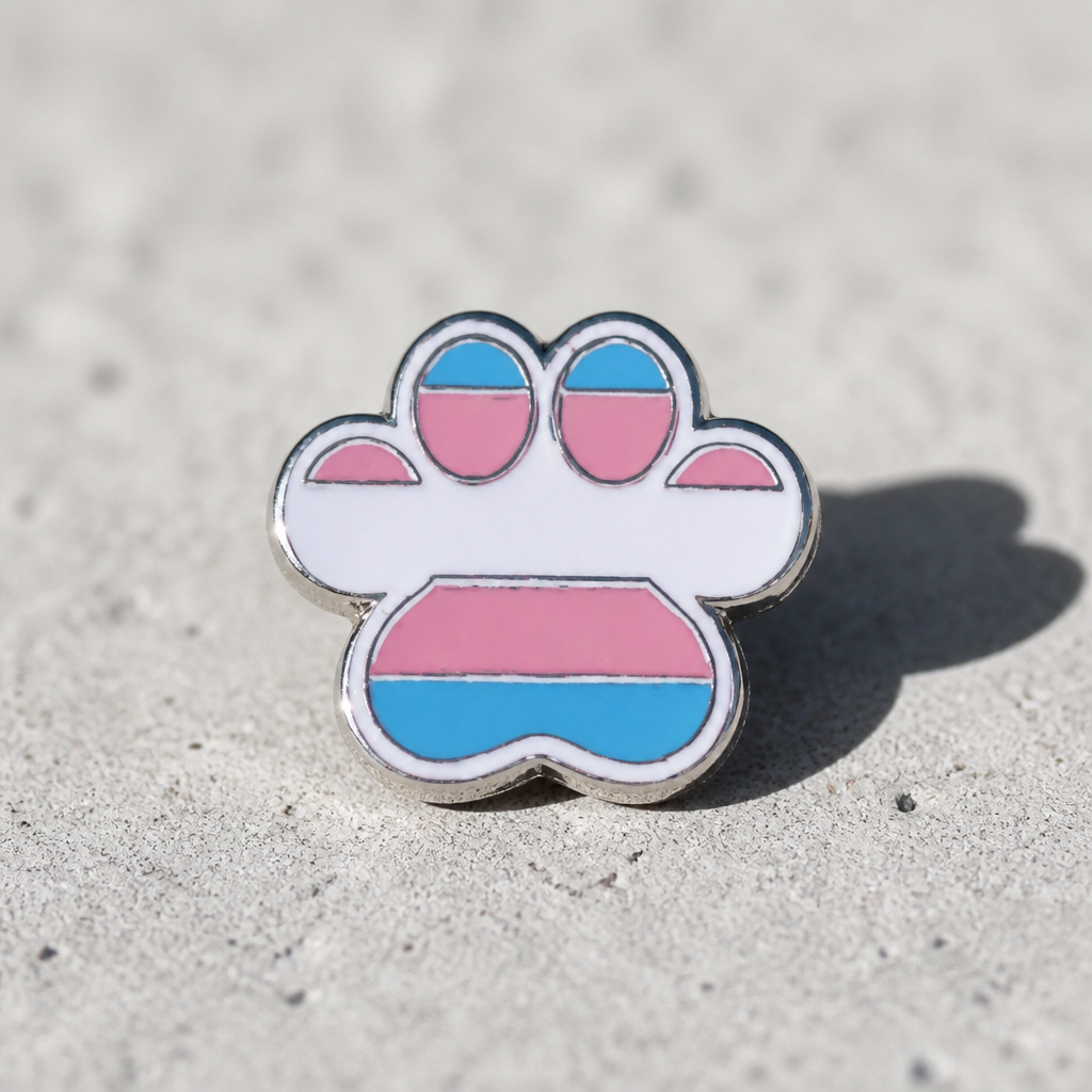 Transgender pride paw print enamel pin with light blue pink and white flag colors on a concrete surface