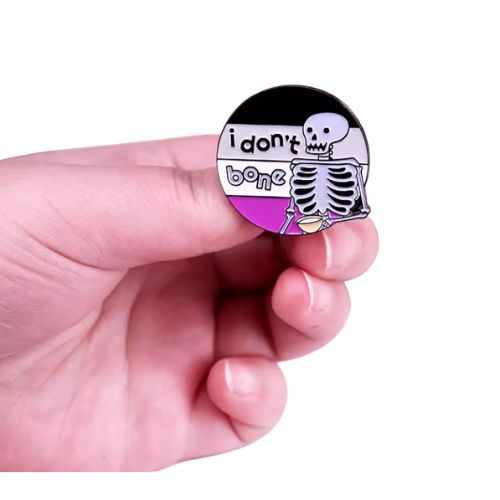 Ace Pride skeleton enamel pin with “I Don’t Bone” text held by a hand