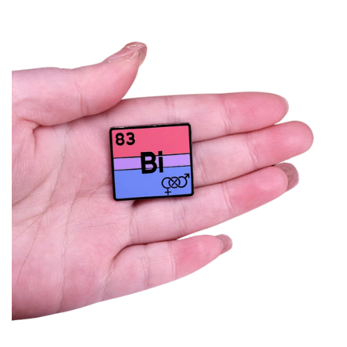 Bisexual pride enamel pin designed like a periodic table element with pink purple and blue flag colors held in a hand