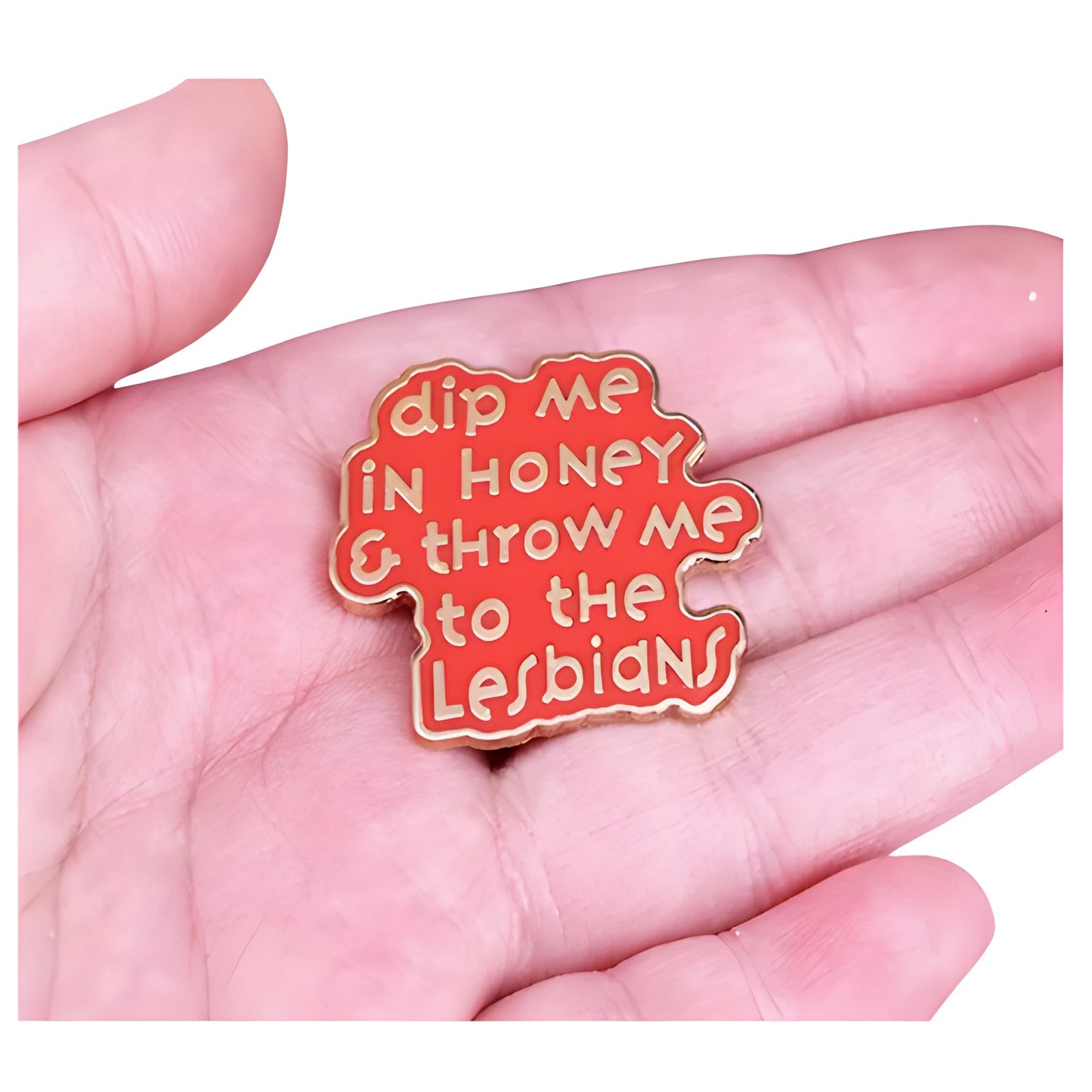 Pink enamel pin with the phrase “Dip Me in Honey & Throw Me to the Lesbians” held in a hand
