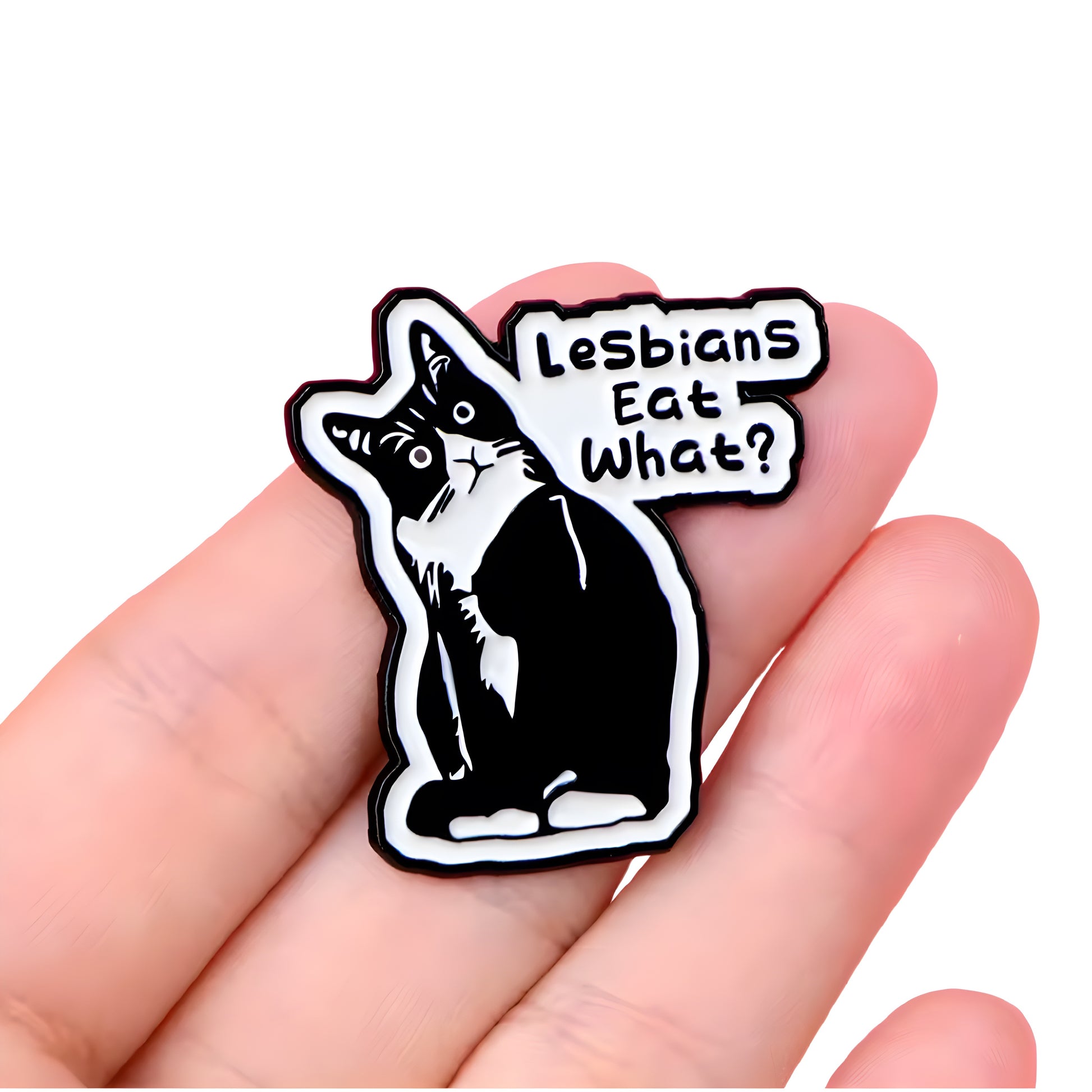 Funny tuxedo cat enamel pin with the phrase “Lesbians Eat What?” held in a hand