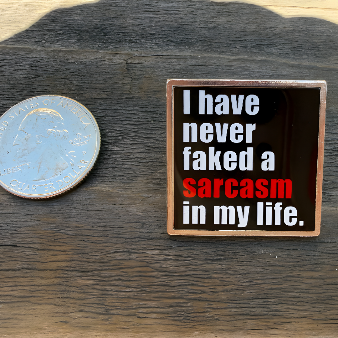 Black enamel pin featuring the phrase "I Have Never Faked a Sarcasm in My Life" with the word "sarcasm" highlighted in red on a wood surface next to a quarter for size reference