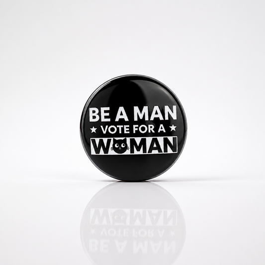 Round enamel pin reading "Be A Man, Vote For A Woman" with bold black and white design