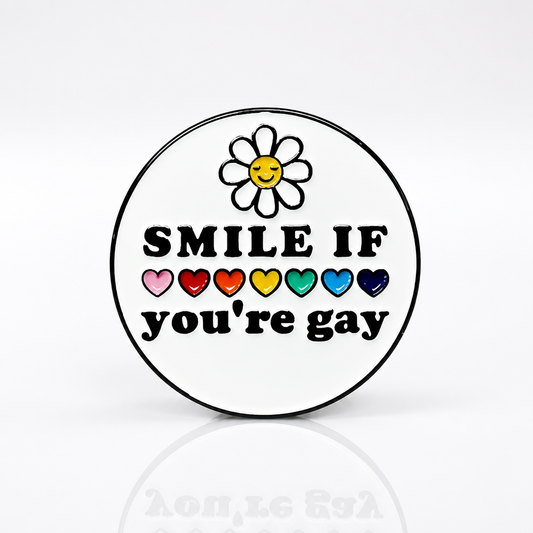 Round hard enamel pin featuring a smiling daisy, rainbow hearts, and the phrase "Smile If You're Gay."