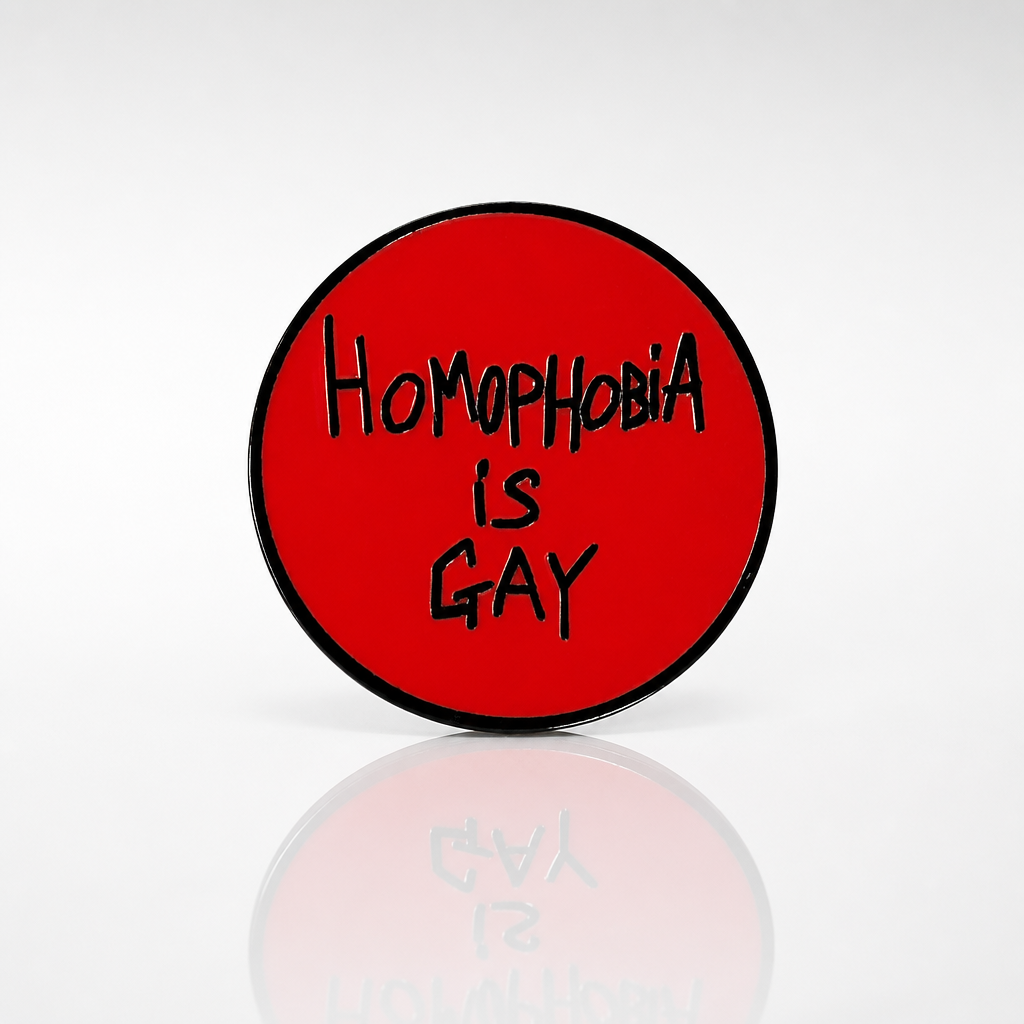 Round red hard enamel pin featuring the phrase "Homophobia Is Gay" in black hand-lettered text.