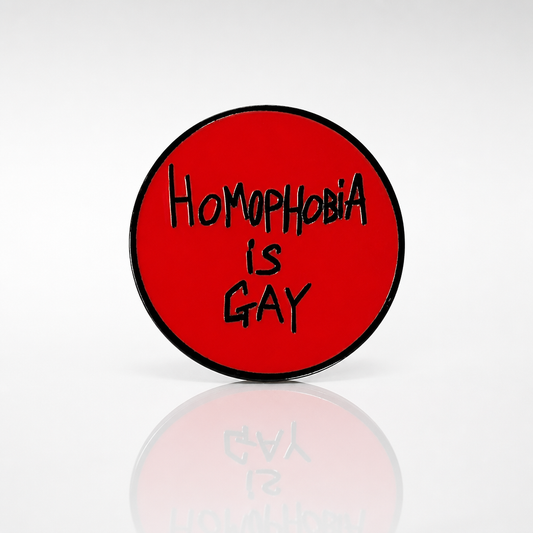 Round red hard enamel pin featuring the phrase "Homophobia Is Gay" in black hand-lettered text.
