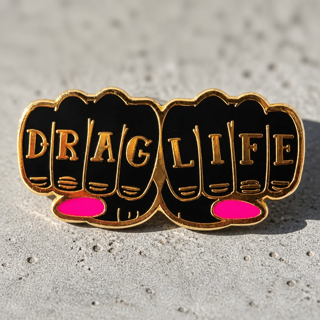 Drag Life enamel pin featuring gold-tone knuckle lettering with pink accent details on a cement surface