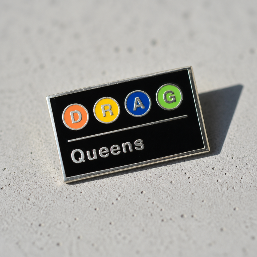 Drag Queens Subway enamel pin featuring colorful transit-style lettering on a black background on a concrete surface