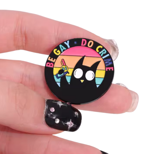 Be Gay Do Crime enamel pin featuring black cat holding rainbow gun with LGBTQ Pride colors held between fingers