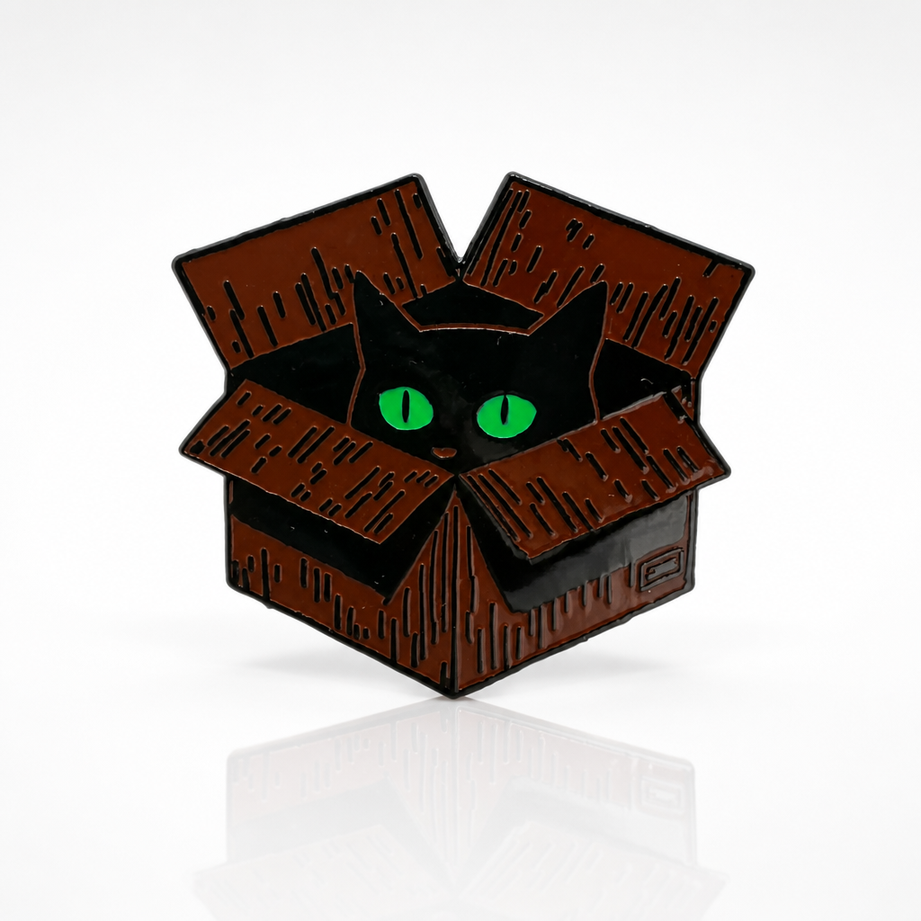 Black cat enamel pin with bright green eyes peeking out from a cardboard box