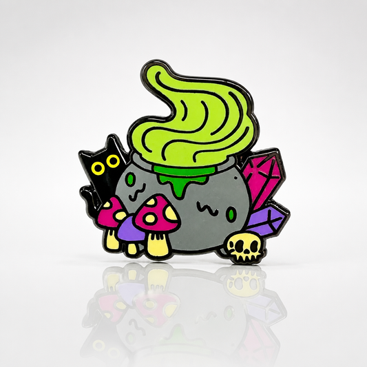 Witchy Cauldron enamel pin featuring a bubbling green cauldron, black cat, crystals, mushrooms, and skull details