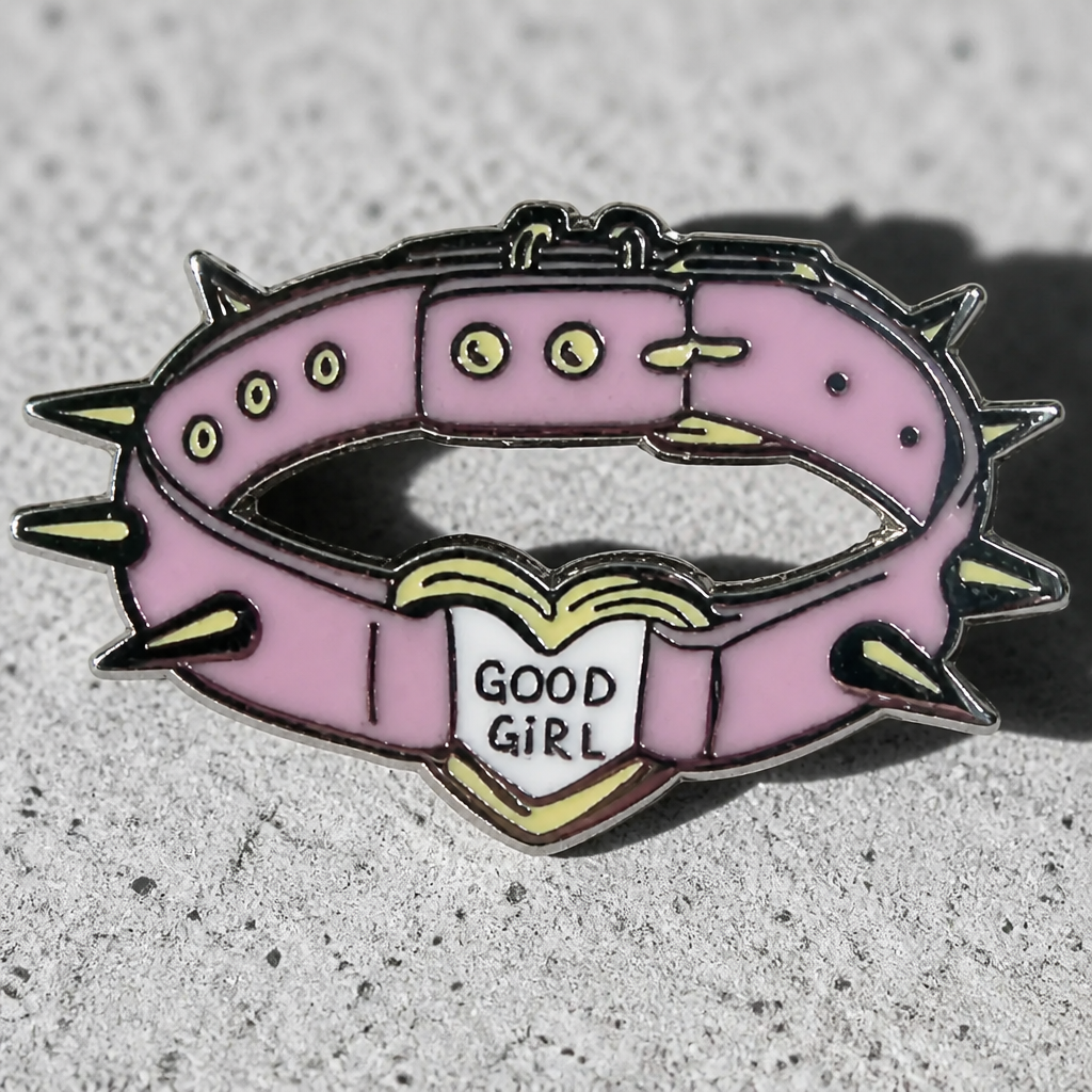 Good Girl Collar enamel pin featuring a pink spiked collar with a heart-shaped charm on a concrete surface