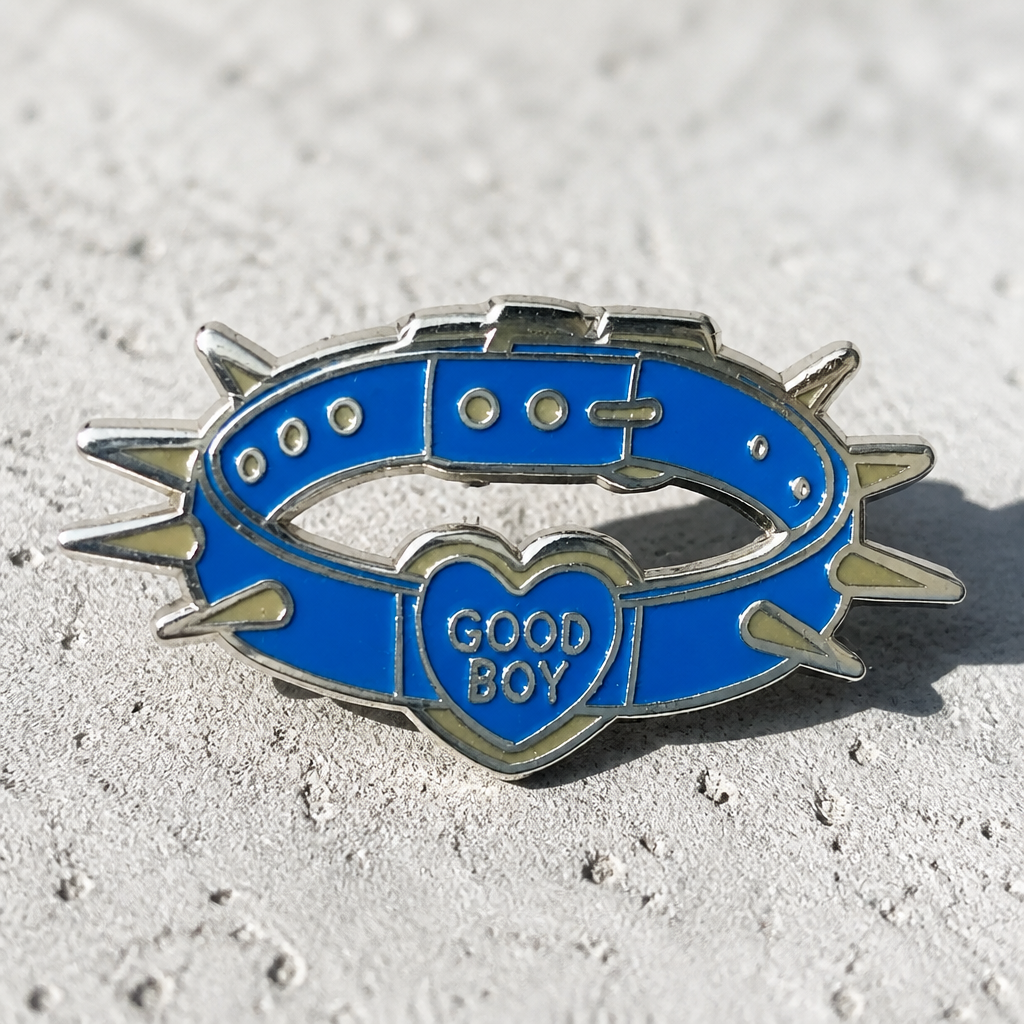 Good Boy Collar enamel pin featuring a blue spiked collar with a heart-shaped charm on a concrete surface