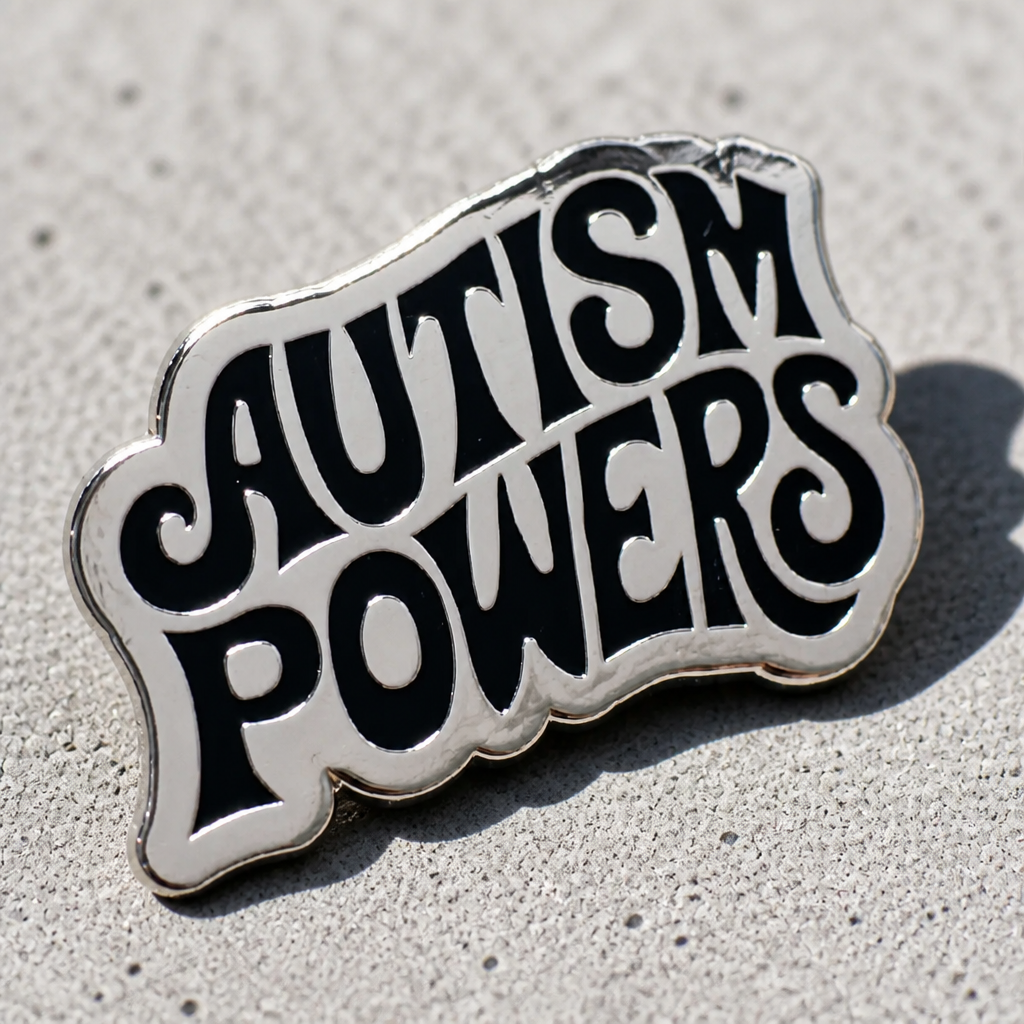 Silver-plated hard enamel pin featuring the words Autism Powers in bold black retro lettering on a concrete background
