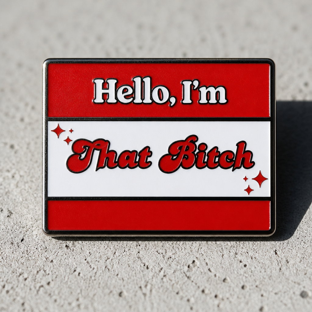 "Hello, I'm That Bitch" soft enamel statement pin inspired by a classic name tag design with bold red, white, and black colors displayed on a concrete surface