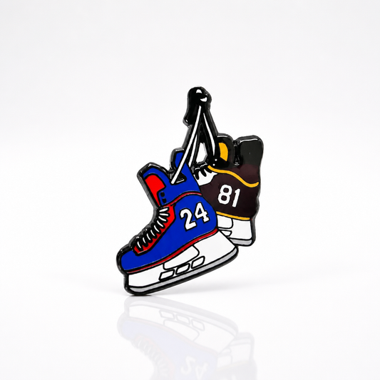 Hard enamel Heated Rivalry hockey skates pin featuring blue and black skates with jersey numbers 24 and 81 hanging together on a white background