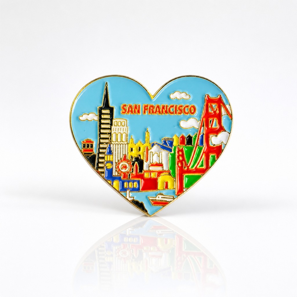 Heart-shaped San Francisco skyline hard enamel pin featuring the Golden Gate Bridge, Transamerica Pyramid, Coit Tower, cable car, and other iconic city landmarks with gold metal accents on a white background