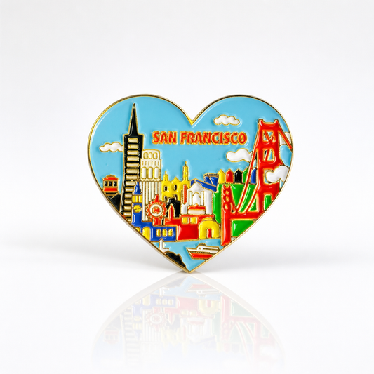 Heart-shaped San Francisco skyline hard enamel pin featuring the Golden Gate Bridge, Transamerica Pyramid, Coit Tower, cable car, and other iconic city landmarks with gold metal accents on a white background