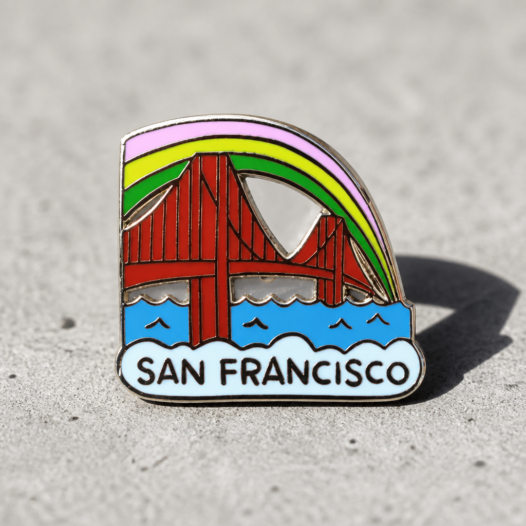 Hard enamel San Francisco Golden Gate Bridge pin featuring a colorful rainbow arch above the bridge with gold metal detailing and a double-post backing displayed on a concrete surface