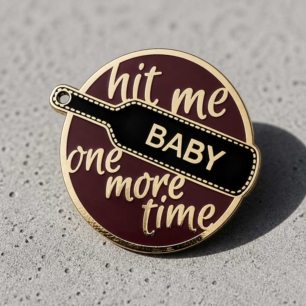 Hit Me Baby One More Time enamel pin with black paddle and gold-tone metal displayed on a concrete surface