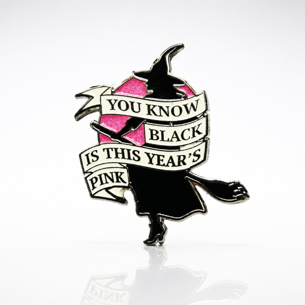 Glitter enamel pin featuring a witch silhouette flying across a pink moon with the phrase Black Is This Year’s Pink