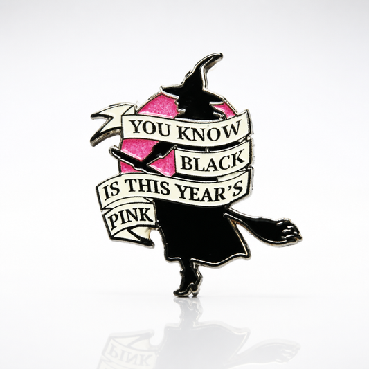 Glitter enamel pin featuring a witch silhouette flying across a pink moon with the phrase Black Is This Year’s Pink