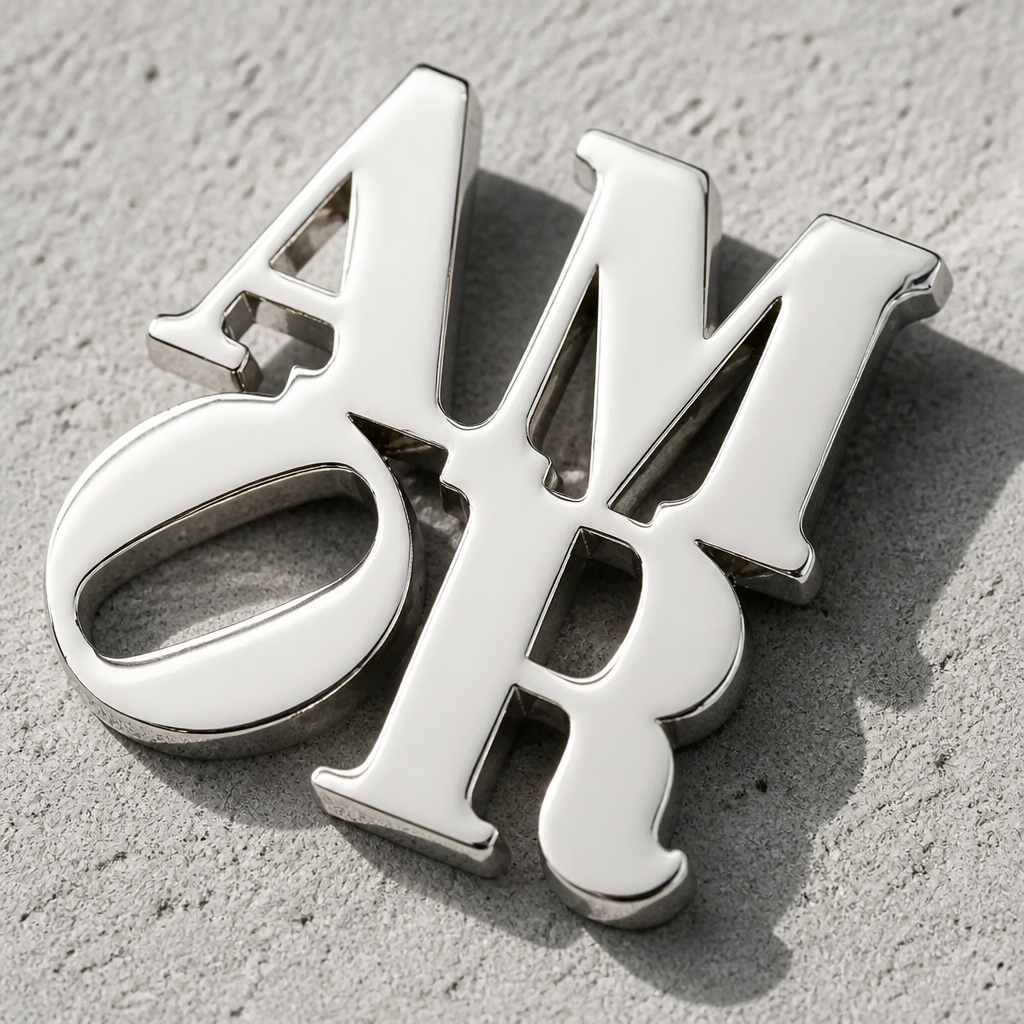 Officially licensed Robert Indiana AMOR enamel pin featuring the iconic stacked lettering in a polished silver finish on a concrete surface
