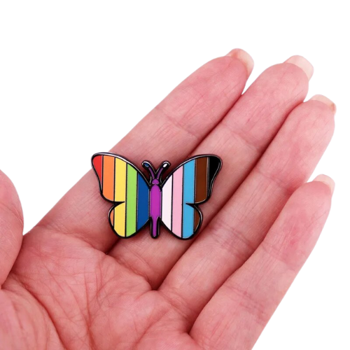 Butterfly enamel pin featuring rainbow and Progress Pride flag colors held in a hand