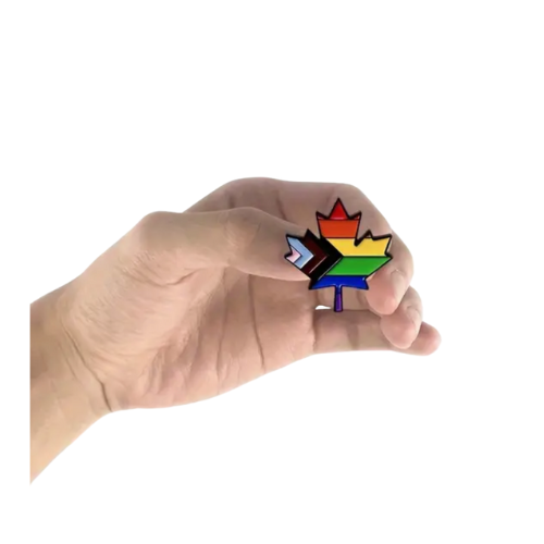 Hand holding a Rainbow maple leaf enamel pin featuring Progress Pride flag colors