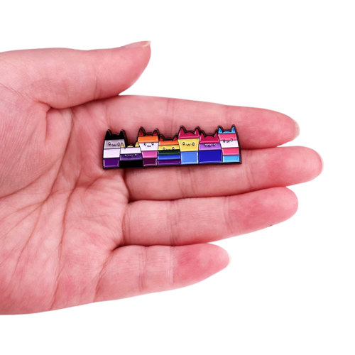 Long enamel pin featuring seven cats in different LGBTQ Pride flag colors held in a hand on white background