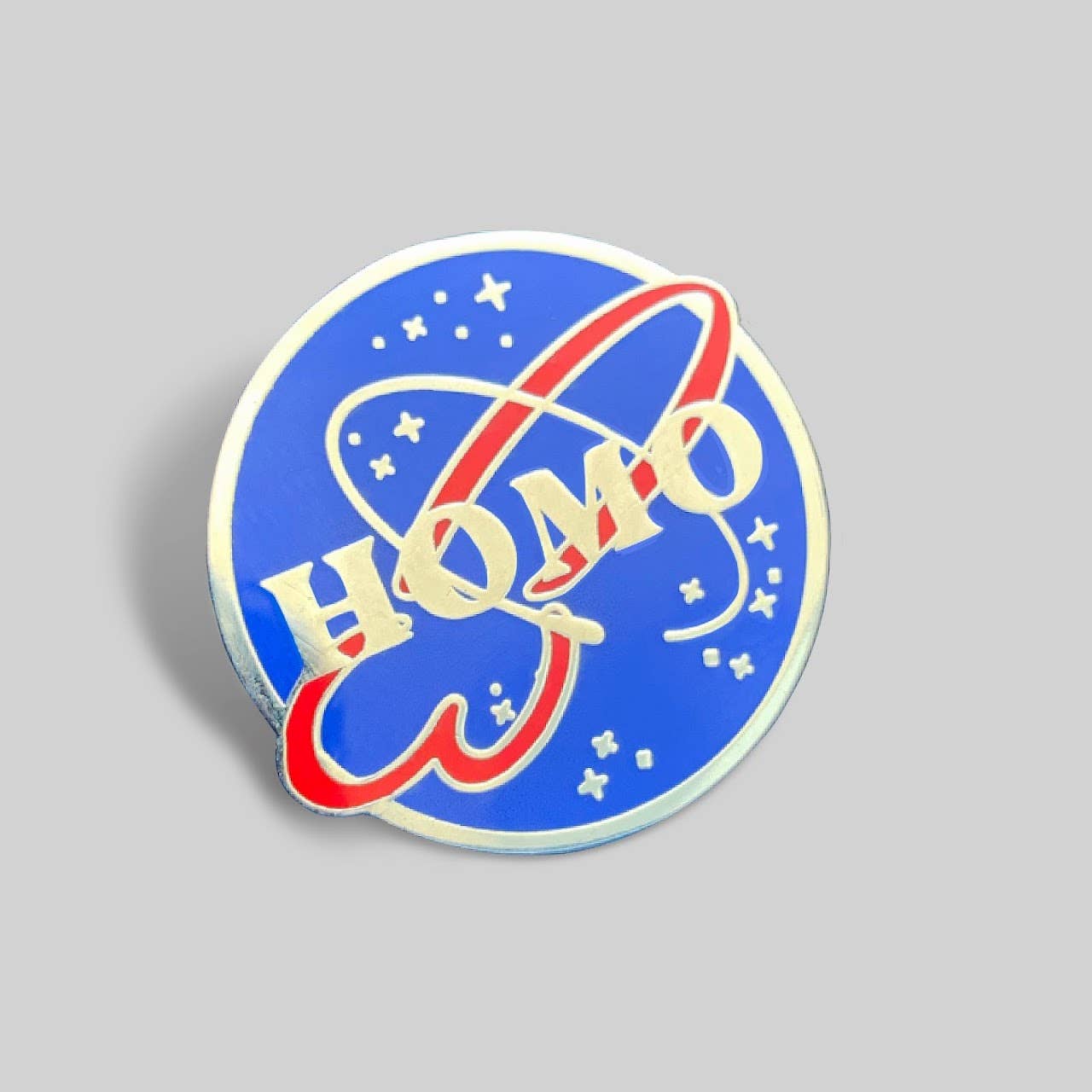 HOMO Space Program enamel pin featuring a retro space-agency-inspired logo design in blue and red