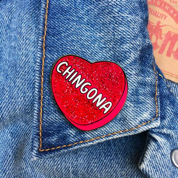 Pink glitter heart enamel pin with Chingona text design on a denim fabric