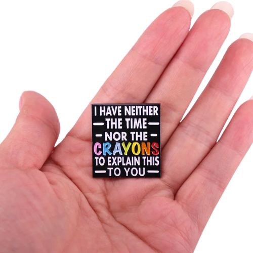 Funny sarcastic enamel pin reading I Have Neither the Time nor the Crayons with colorful lettering held in a hand against a white background