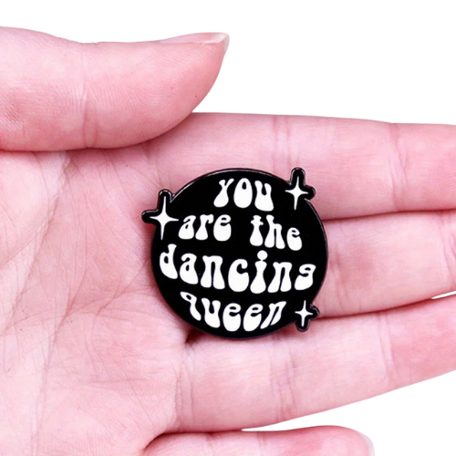 Retro Dancing Queen enamel pin with bold disco-inspired lettering and sparkles held in a hand