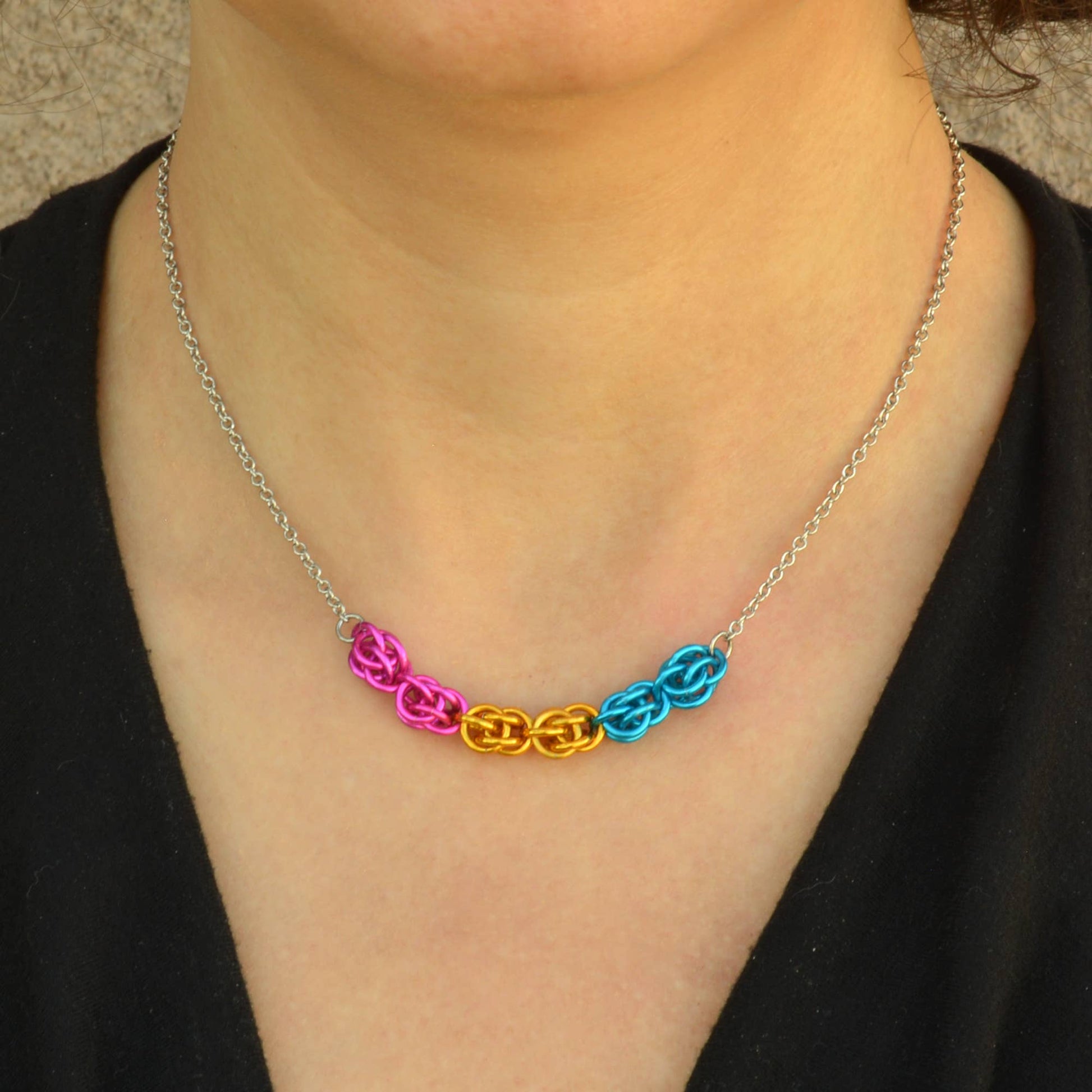 a close-up of a person wearing a Hand-linked pansexual pride chainmail necklace featuring pink, yellow, and blue aluminum rings on an adjustable stainless steel chain.