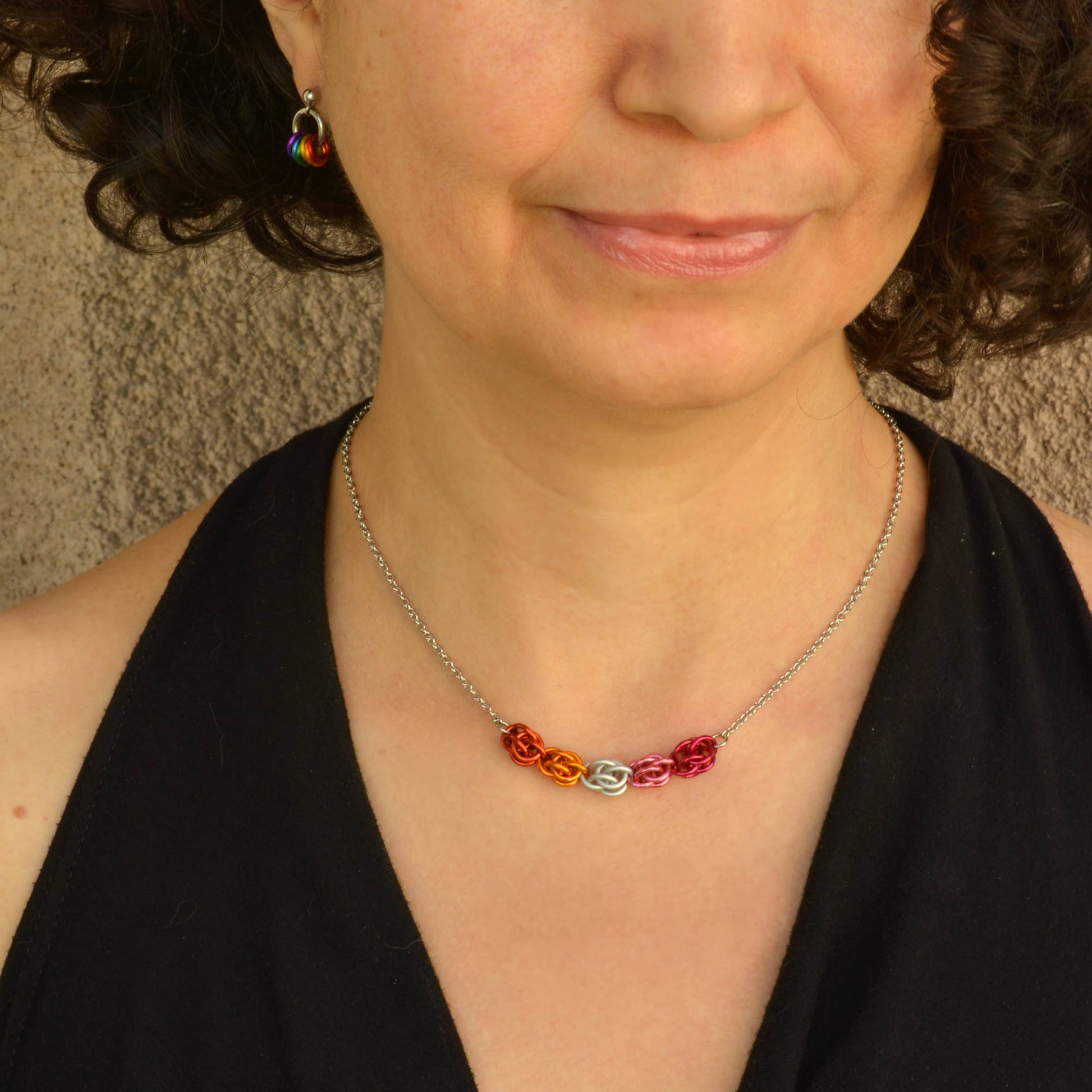 a close-up of a woman wearing a Hand-linked lesbian pride chainmail necklace featuring orange, white, pink, and magenta aluminum rings on an adjustable stainless steel chain.