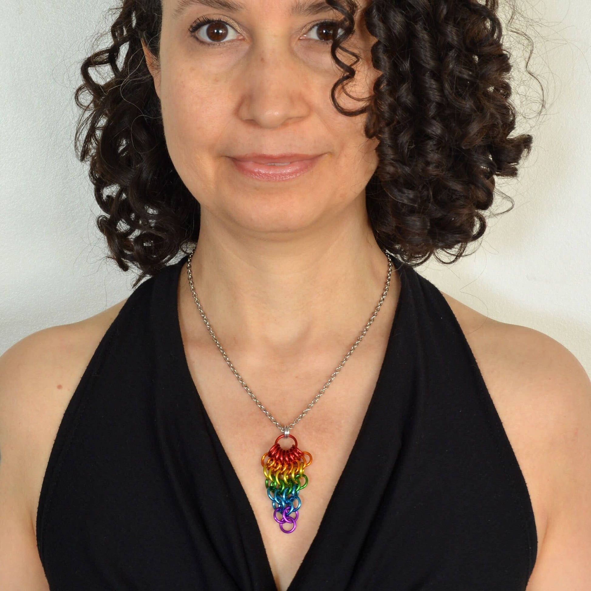 a woman wearing a Hand-linked rainbow chainmail cluster pendant featuring cascading aluminum rings on an adjustable stainless steel chain.