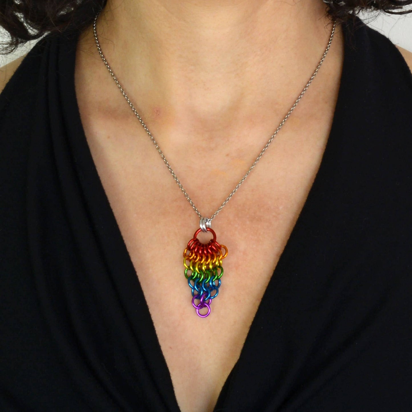 a close-up of a person wearing a Hand-linked rainbow chainmail cluster pendant featuring cascading aluminum rings on an adjustable stainless steel chain.