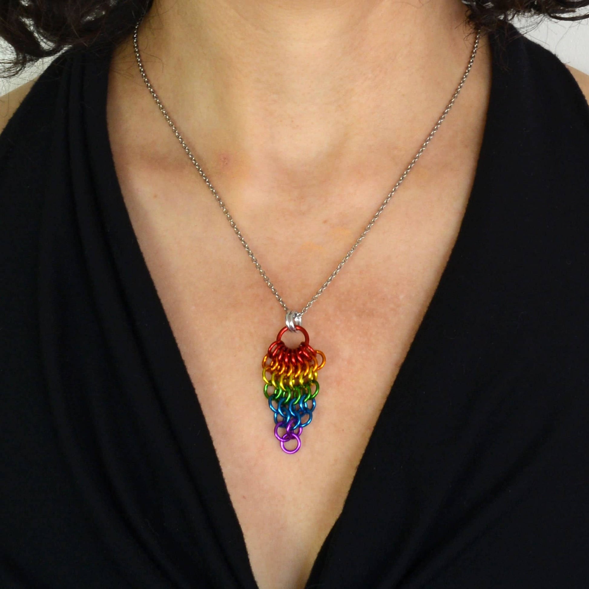a close-up of a person wearing a Hand-linked rainbow chainmail cluster pendant featuring cascading aluminum rings on an adjustable stainless steel chain.