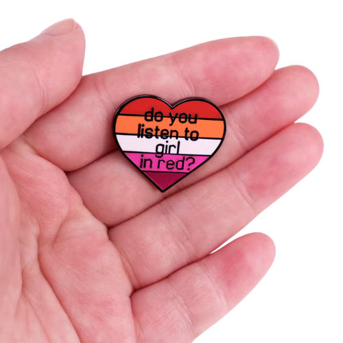 Heart-shaped lesbian Pride enamel pin reading “Do You Listen to Girl in Red?” held in a hand
