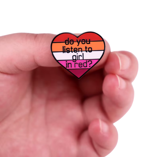 Heart-shaped lesbian Pride enamel pin reading “Do You Listen to Girl in Red?” held in a hand against a white background