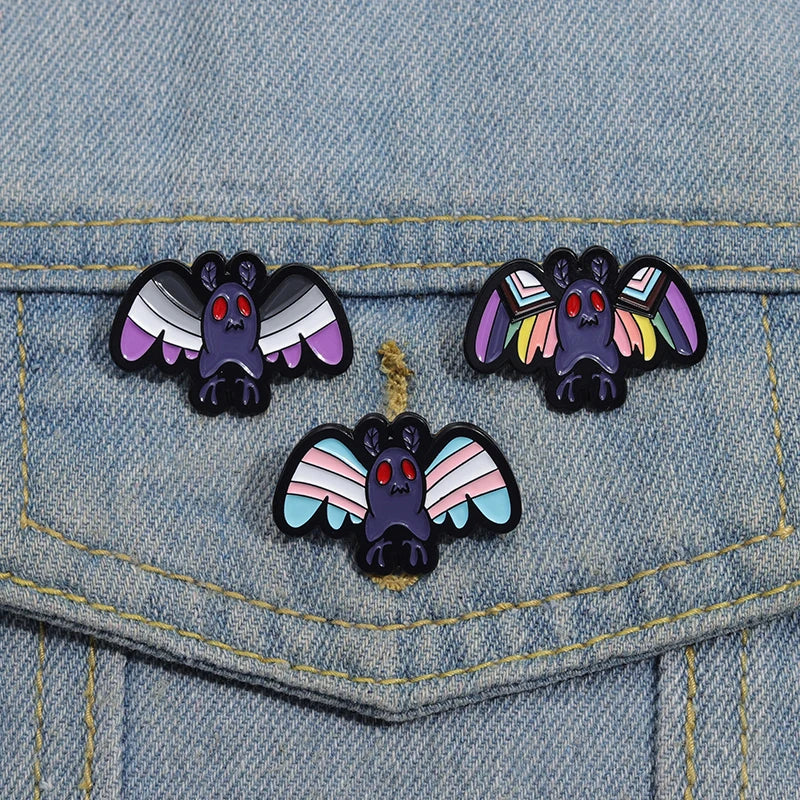 Mothman Pride enamel pins 3 of them, featuring transgender Pride flag colors, Ace Pride flag colors and the 3rd rainbow pride flag colors on a denim fabric