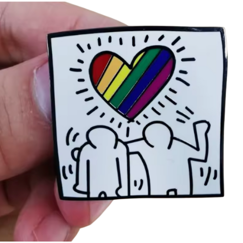 Pop art inspired enamel pin featuring abstract figures beneath a rainbow heart
held by a hand