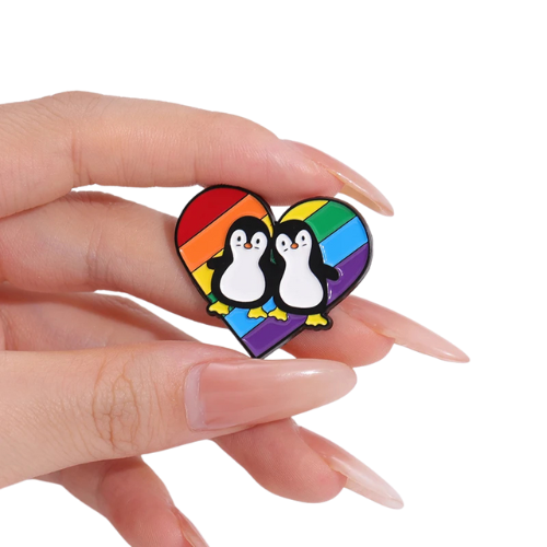 Cute penguin couple enamel pin standing on a rainbow pride heart background held by a hand