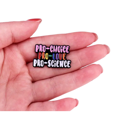 Pro-Choice Pro-Love Pro-Science enamel pin with colorful progressive statement lettering held in a hand