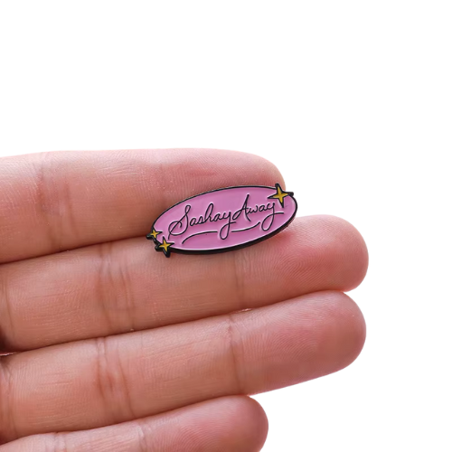 Pastel pink Sashay Away enamel pin with glamorous script lettering and star accents between fingers on a white background