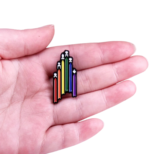Rainbow sci-fi inspired enamel pin with colorful Pride flag insignia design in a hand on a white background